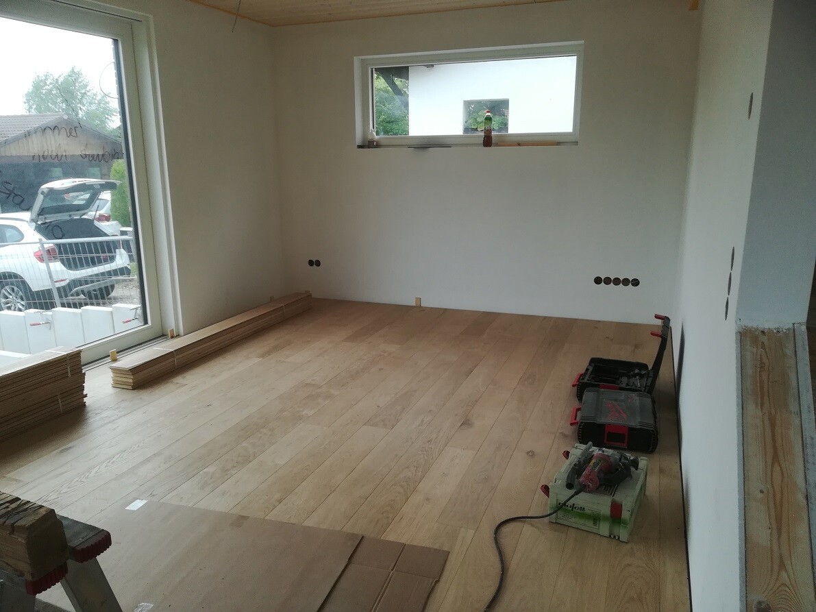 Room under construction with wooden floor, tools, and wooden moldings; large window on the back wall