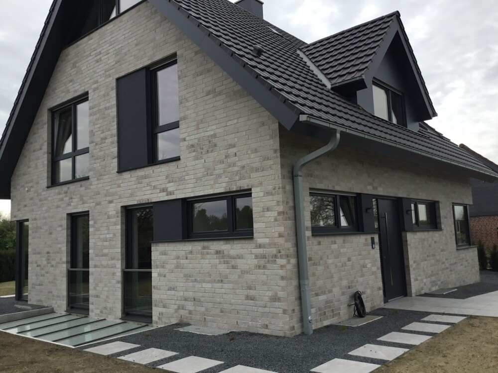 Modern house made of light gray bricks, dark window frames, pitched roof.