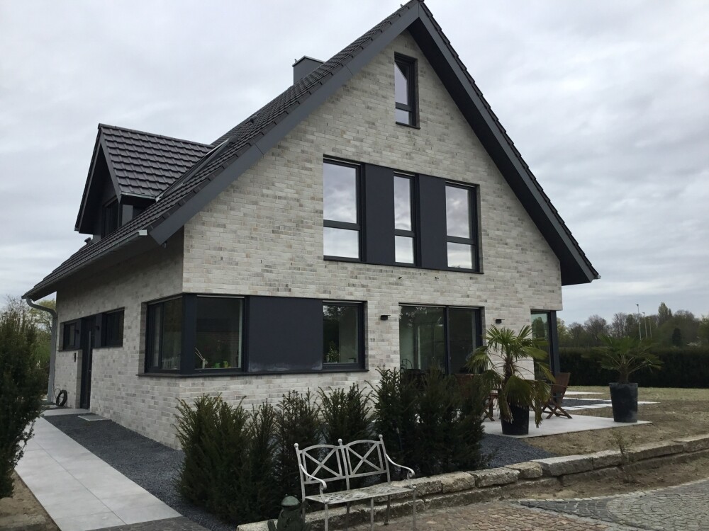 Modern two-story house made of light bricks, gable roof, black window frames, patio.