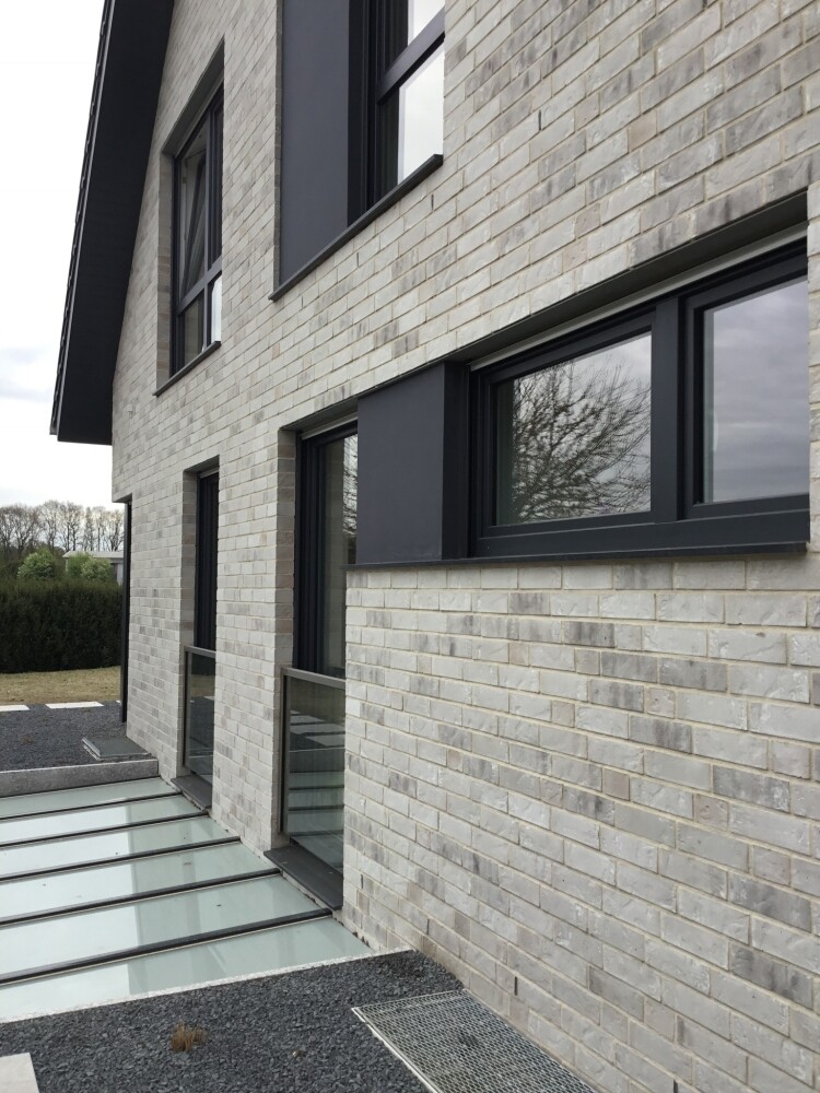 Modern two-story facade made of light gray bricks with black window frames.