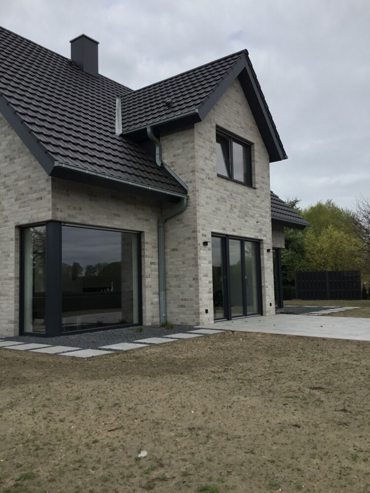Modern house facade made of light bricks, large glass windows, and terrace area.