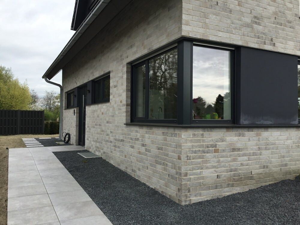 Exterior view of a modern house with light gray bricks and large black window frames.