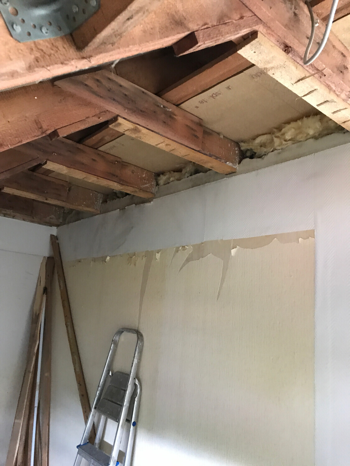 Offene Deckenbalken mit Daemmaterial und Leiter im renovierungsbeduerftigen Innenraum
