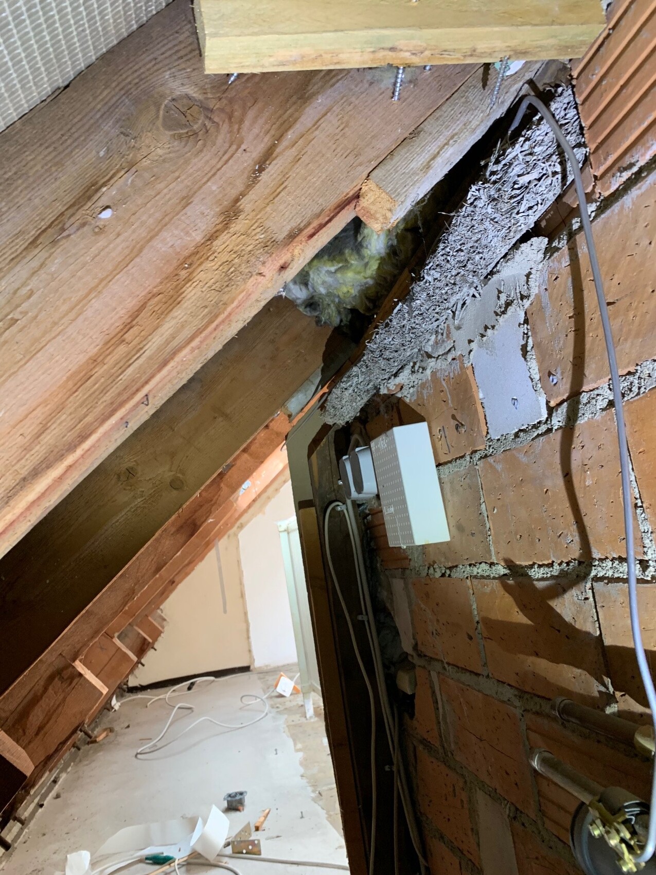 Unfertiges Dachgeschoss mit Holzbalken, Dämmung und Kabeln an Bruchsteinwand.
