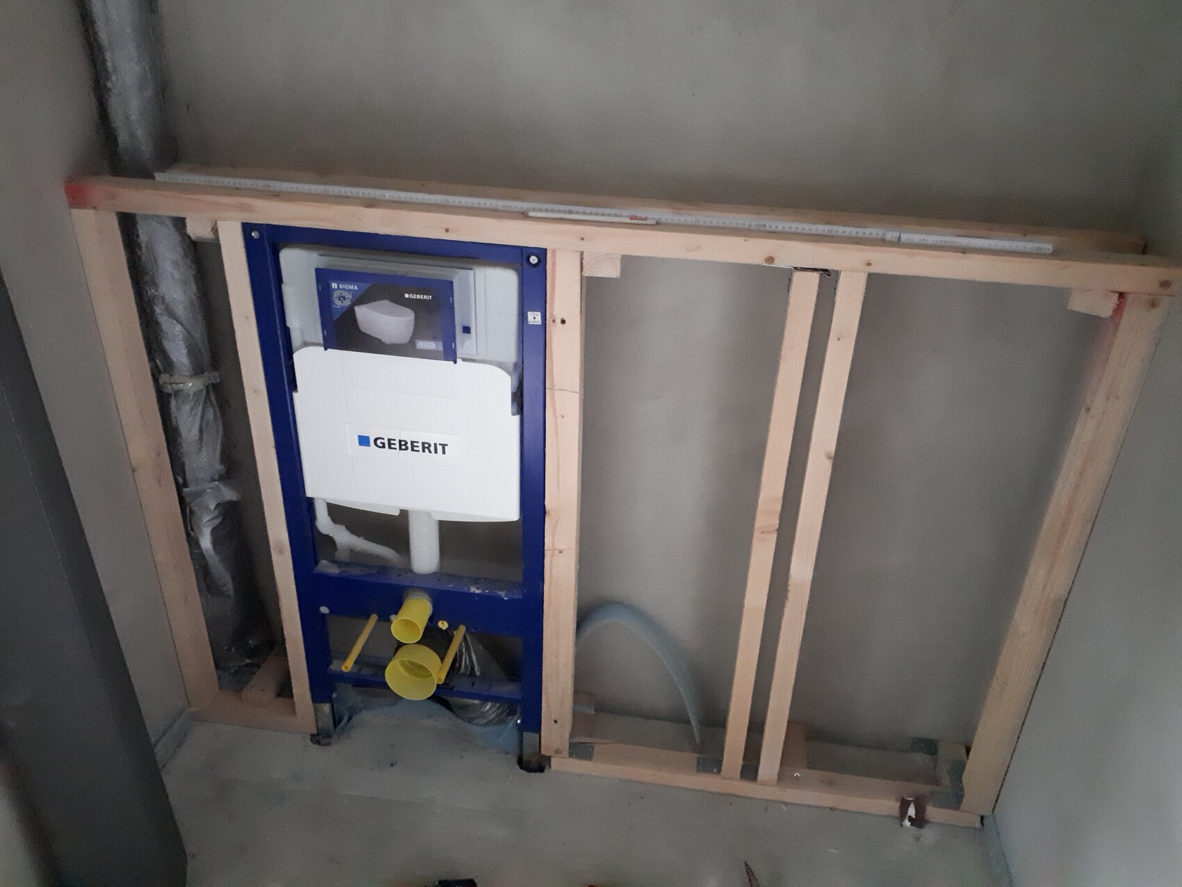 Geberit flush tank wall installation behind timber stud frame, visible pipes and components.