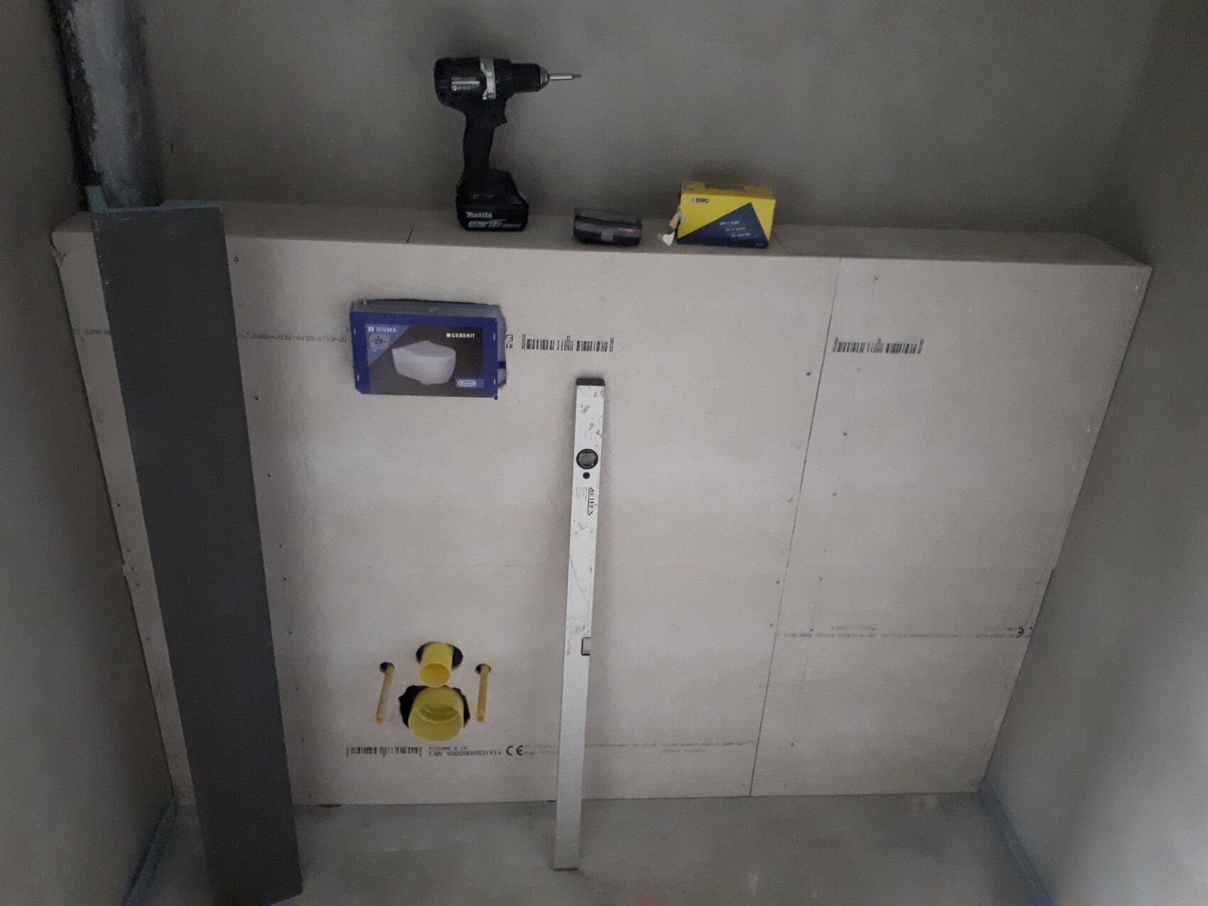 Construction wall with installation panel, drill, toolbox, yellow ball valve, and spirit level.