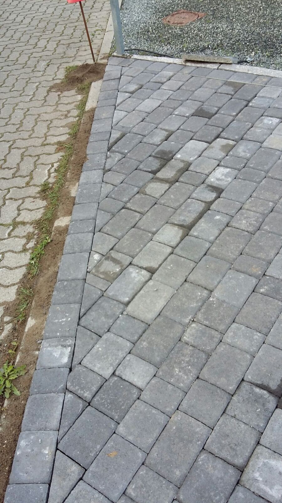 Paved area with gray concrete stones arranged diagonally, bordering earth strip.