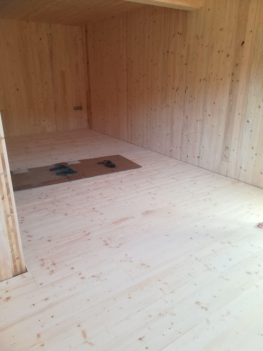 Empty room with wood paneling on walls and wooden floor; shoes placed on a box.