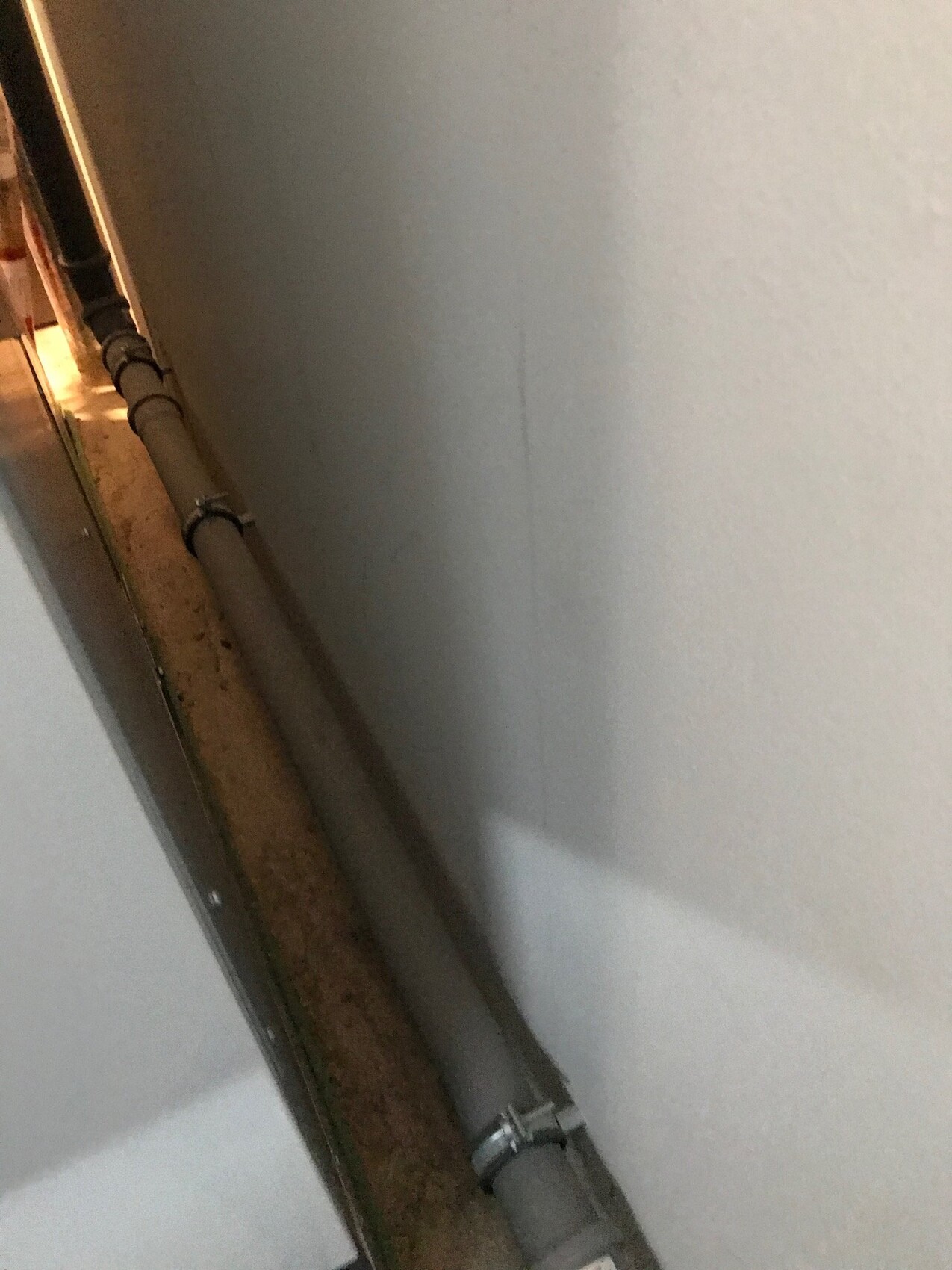 Gray wall with gray pipe held by brackets; left door opening visible.