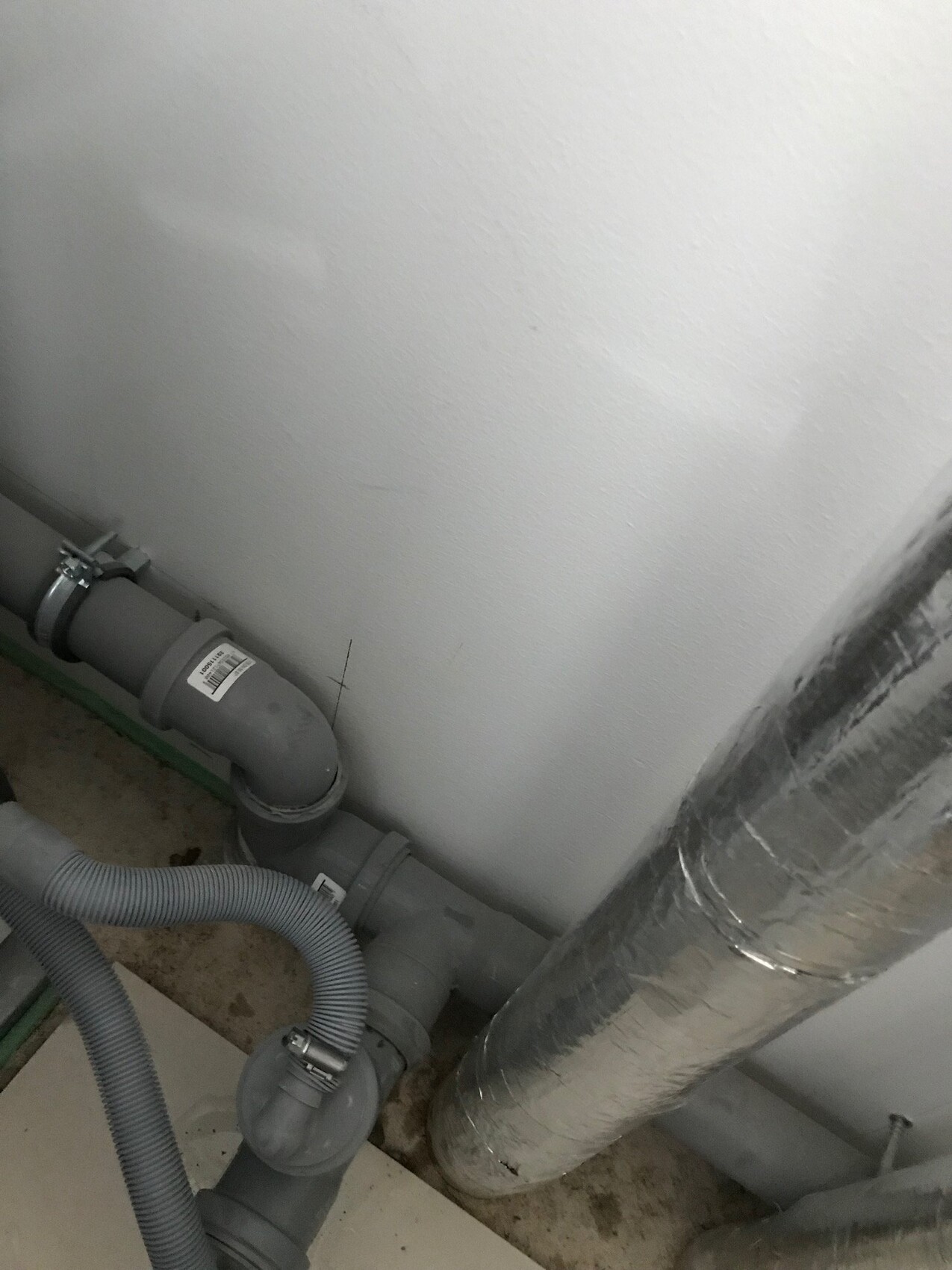 Gray PVC pipes with bends, flexible hose and silver insulated line next to wall.