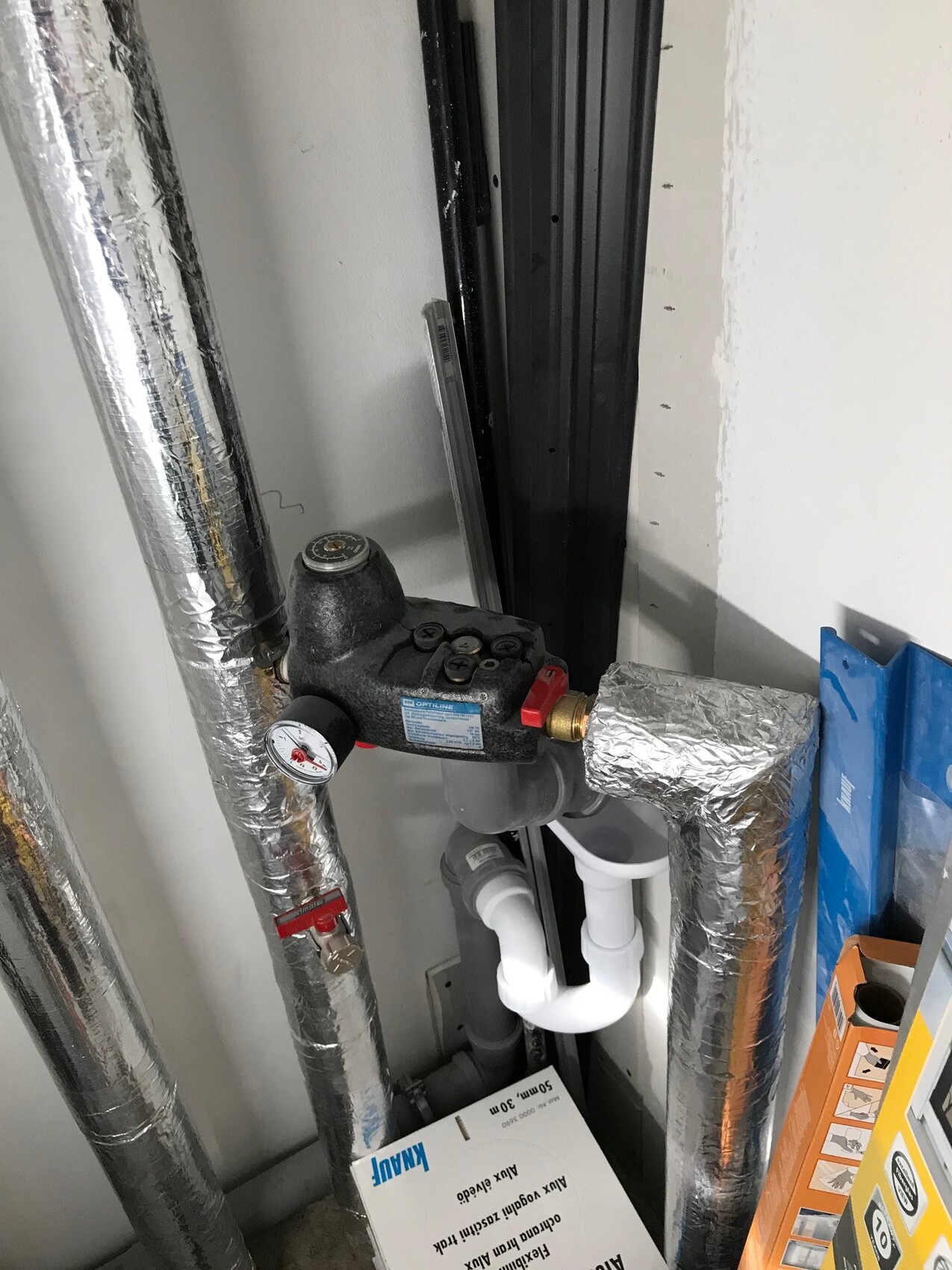 Pressure regulator and insulated piping in utility room, visible PVC drain pipe.