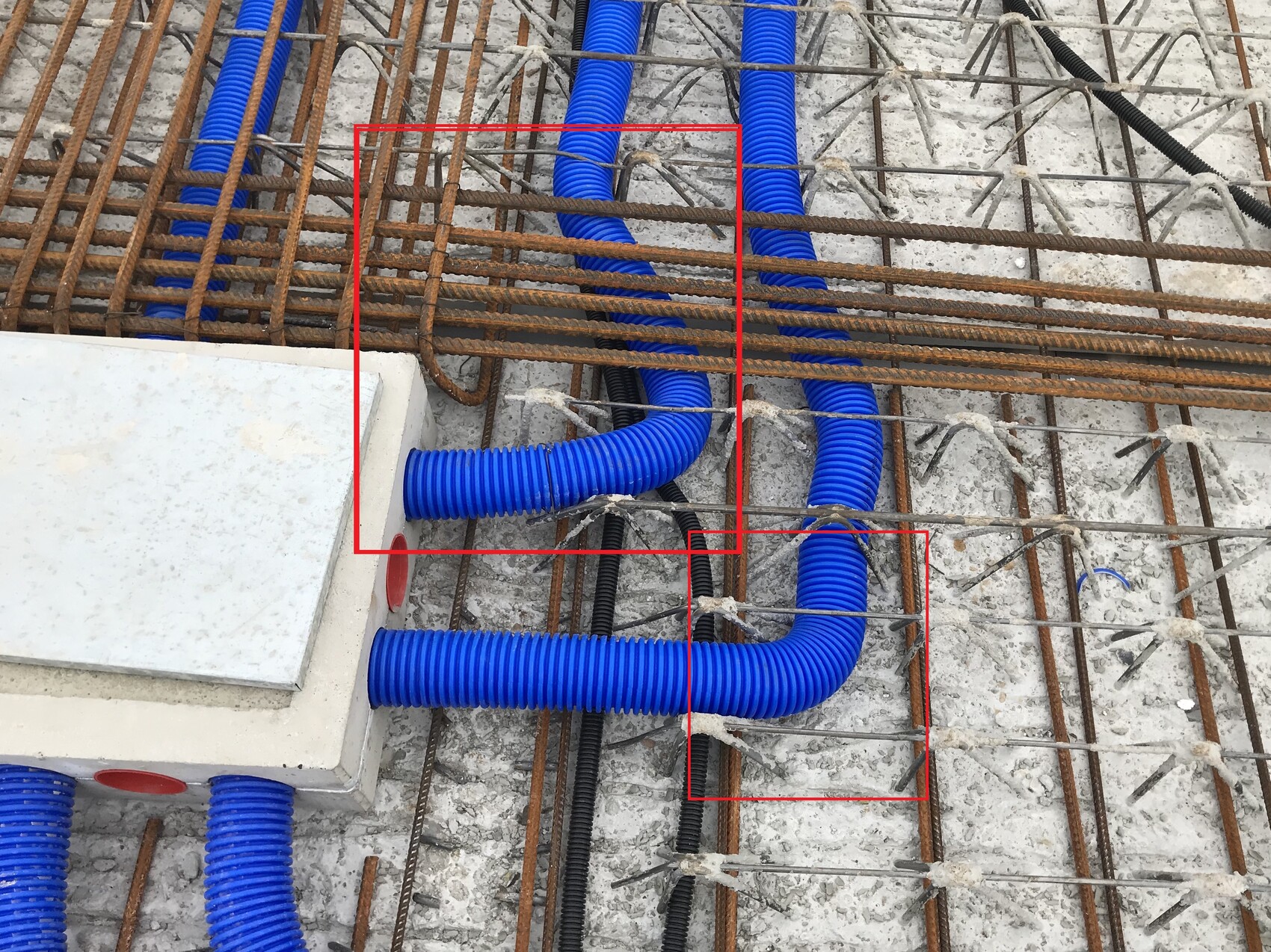 Construction site: Blue flexible cable ducts run through reinforcement steel on a concrete floor.