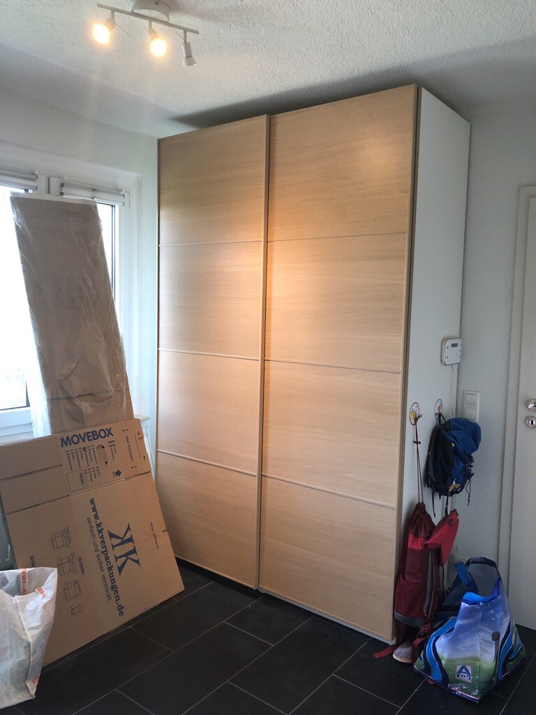 Large light wood-colored wardrobe with sliding doors in the hallway; boxes and backpacks next to it.