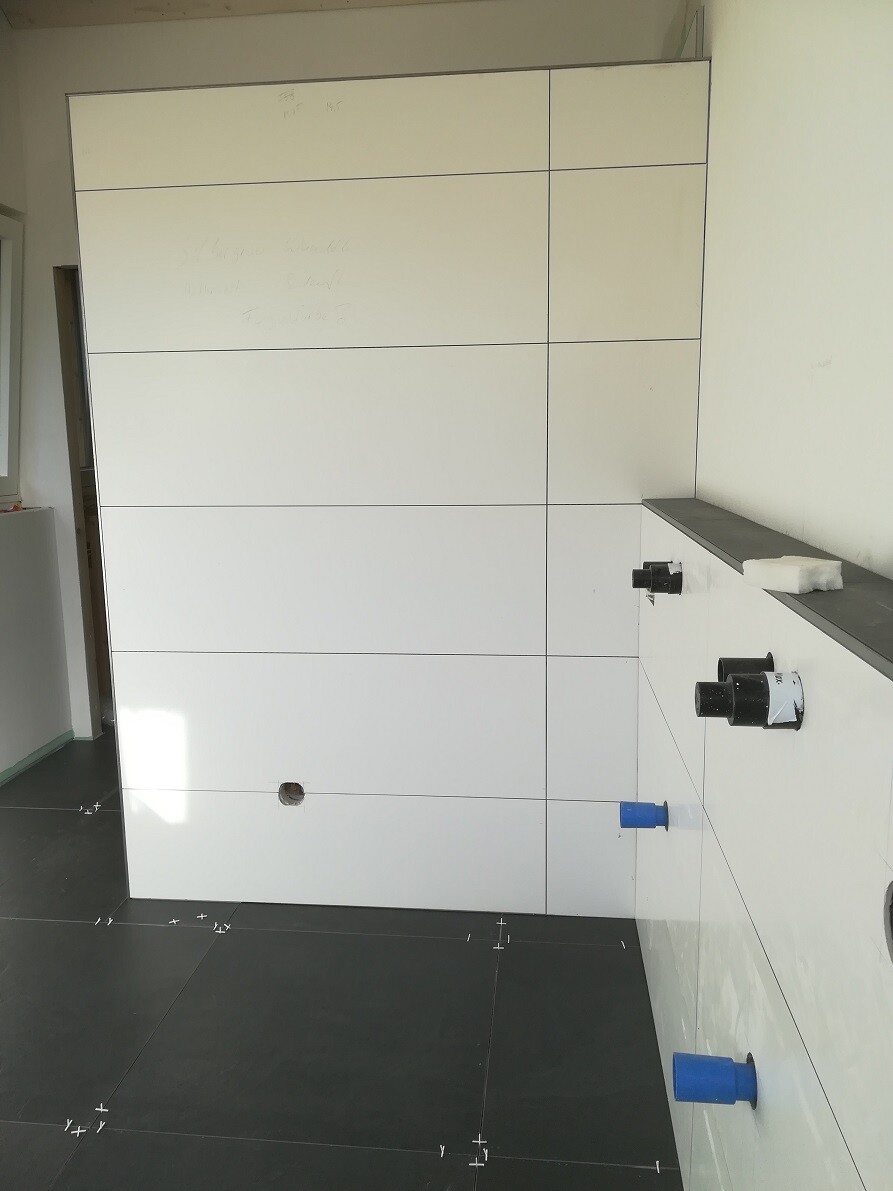 White tiled wall with grout lines; blue pipes protruding from the wall, dark floor.