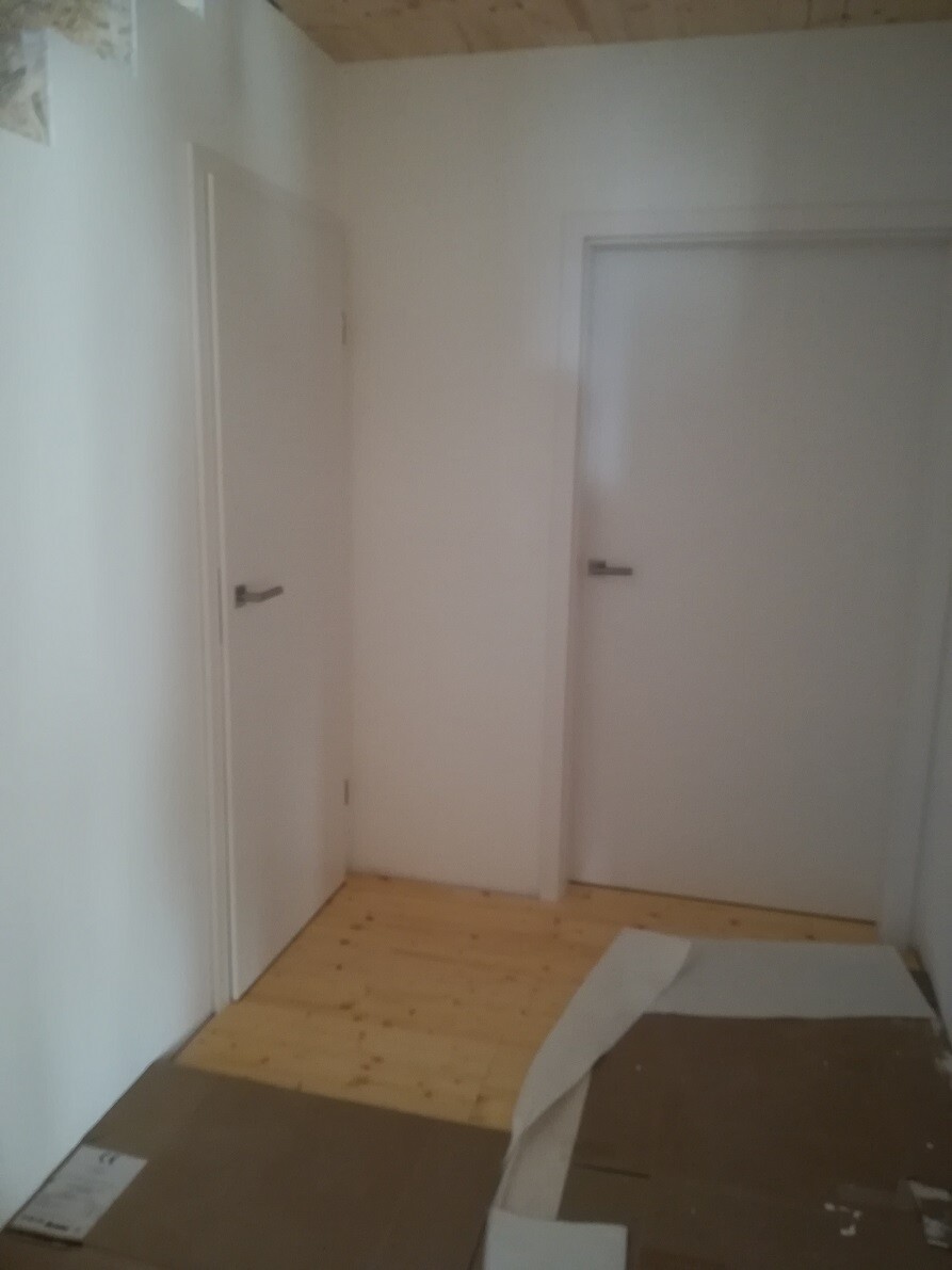 Hallway with white interior doors, light wooden floor, and cardboard pieces on the floor.