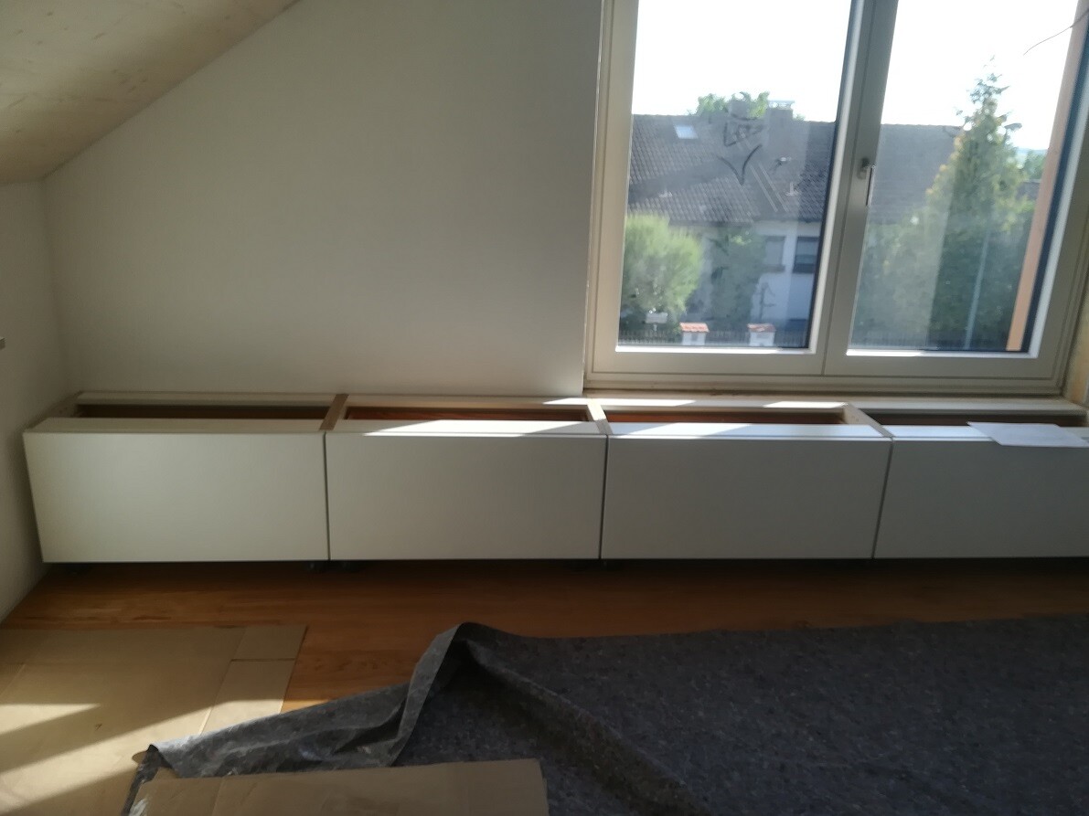 Bright room with four white base cabinets under a large window, wooden floor.