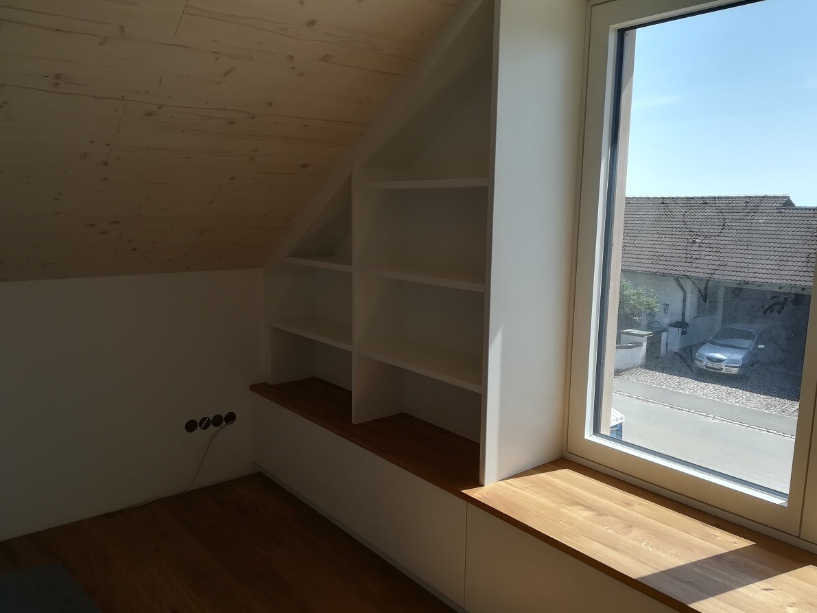 Bright room with slanted wooden roof, white shelves, and wooden windowsill at the window.
