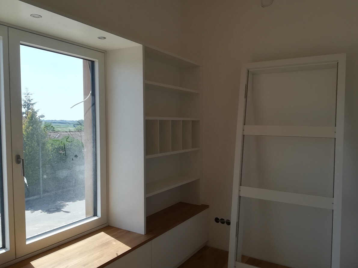 Bright interior with large window, white shelving system with compartments and a door leaning against the wall