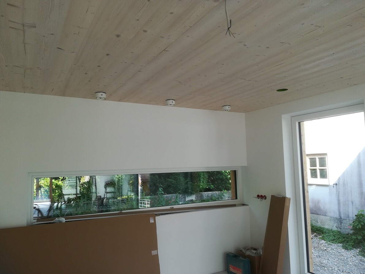 Interior under construction: wooden ceiling, long window front, building components/tool stacks, Makita case.
