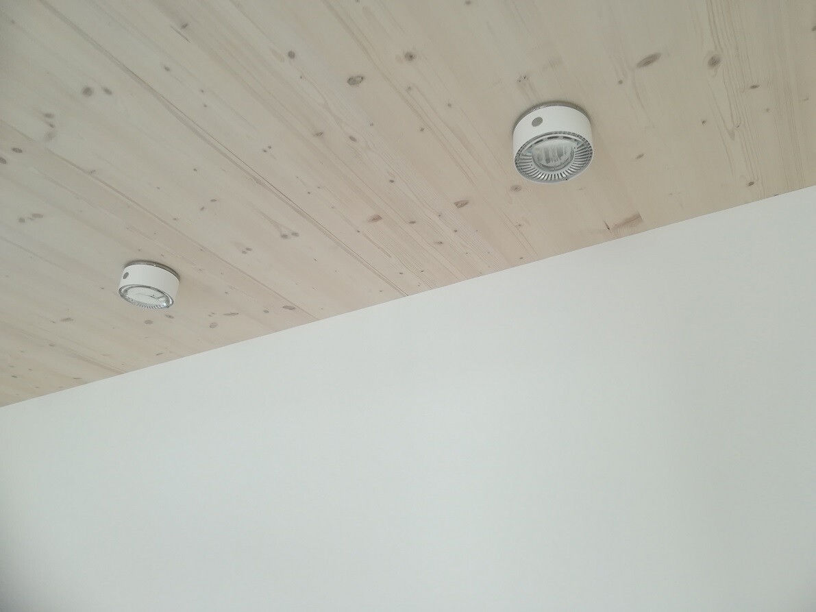 Wooden ceiling with two round white ceiling lights over a light wall.