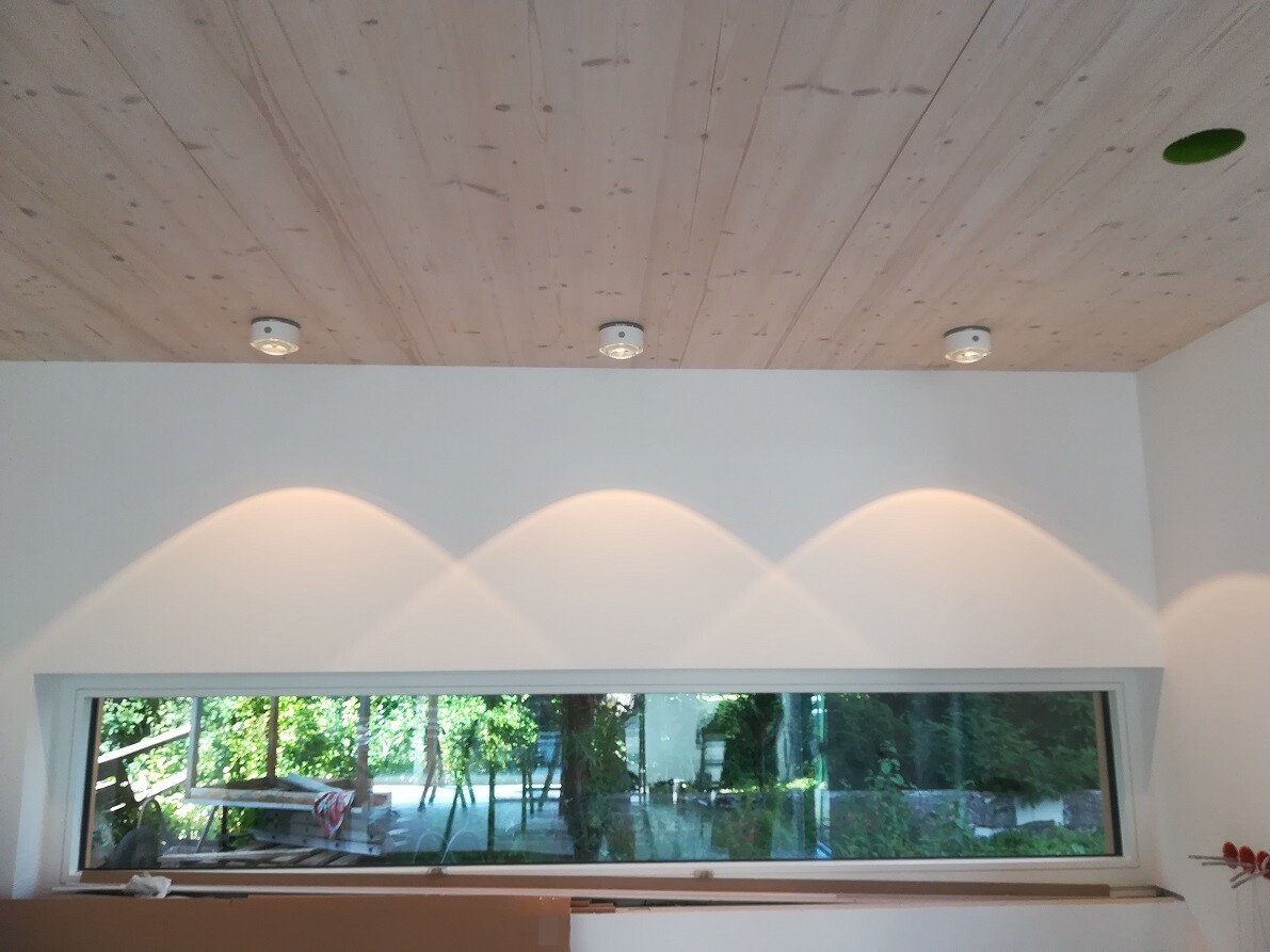 Bright interior with wooden beam ceiling, three ceiling spots, and long horizontal window with garden view.
