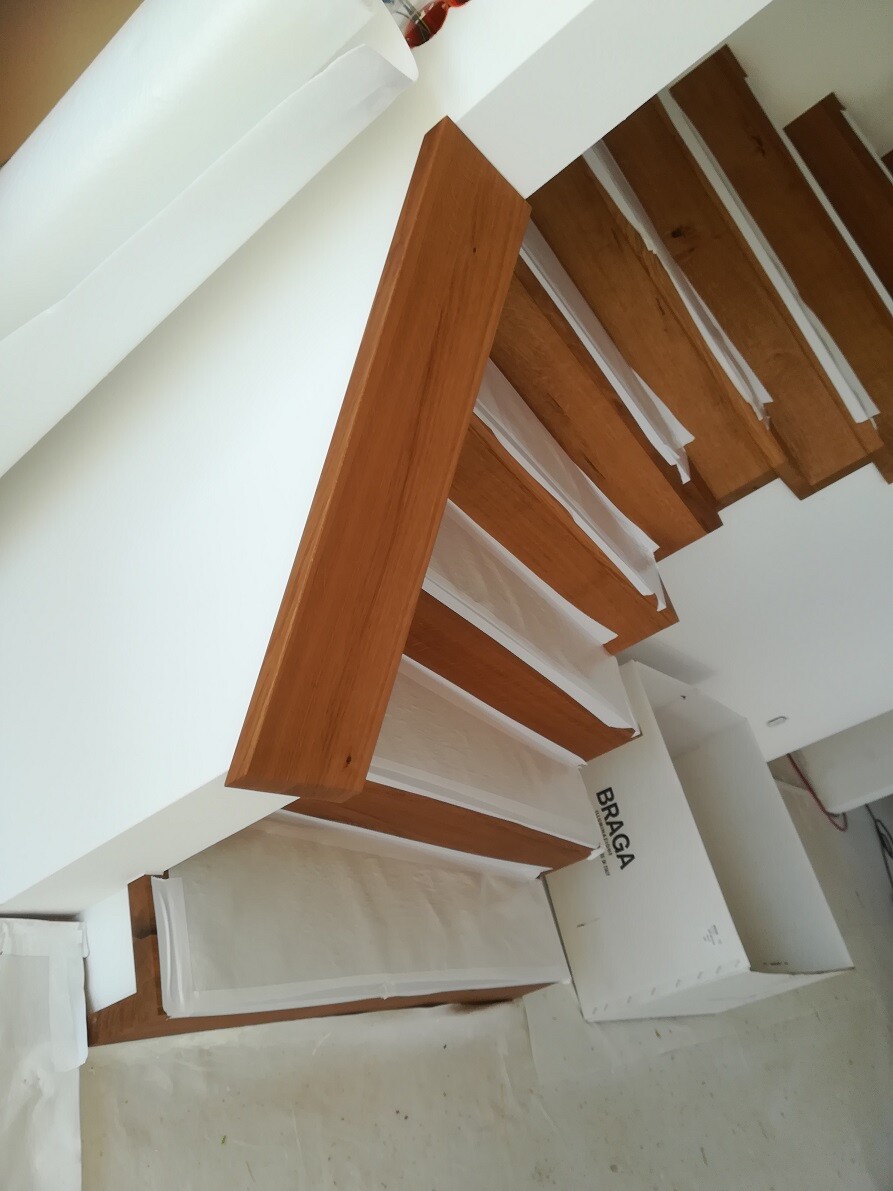 Modern indoor staircase made of brown wooden steps along a white wall.