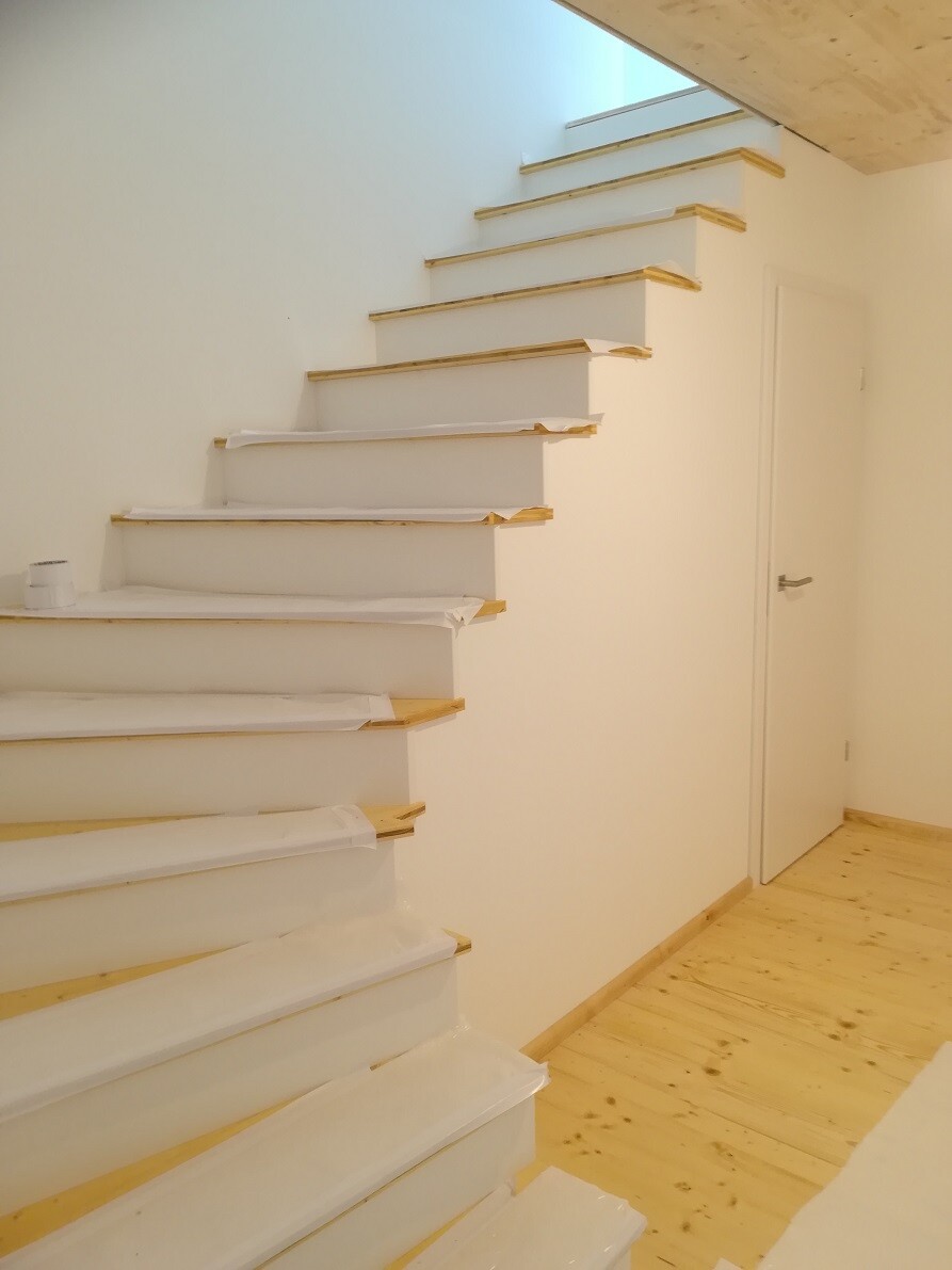 White modern staircase along the wall with wooden edges, protective film on the steps, door on the right.