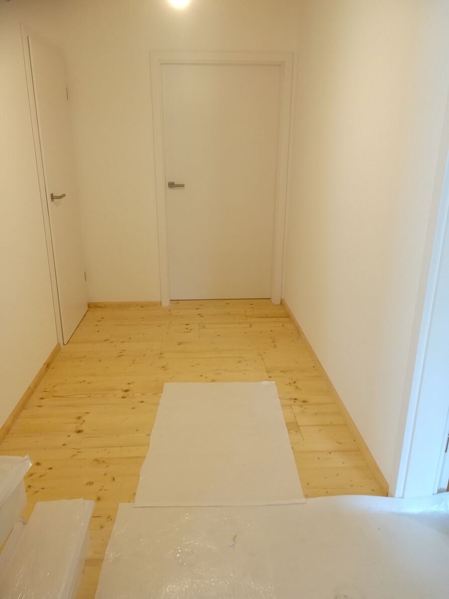Bright hallway with light wooden floor, two white doors, protective covering on the floor.