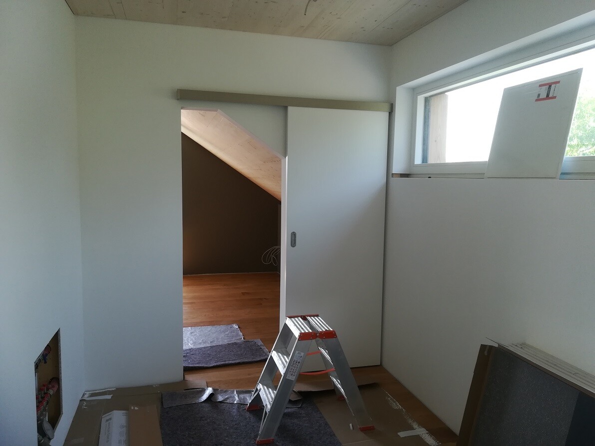Renovation room: open sliding door, ladder, building materials, dark attic area in the background.