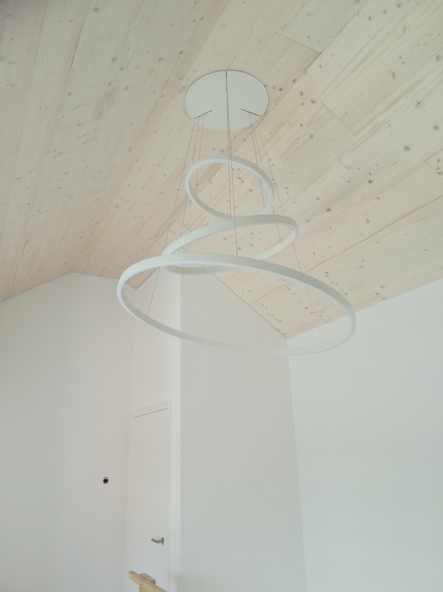 Modern pendant light with three continuous rings on a wooden beam ceiling, bright room.