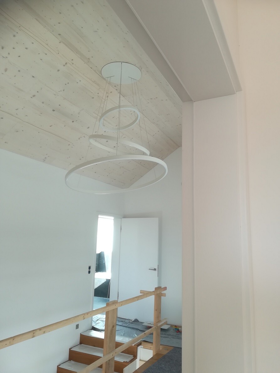 Bright interior with pendant light made of rings, temporary wooden railing on the stairwell.