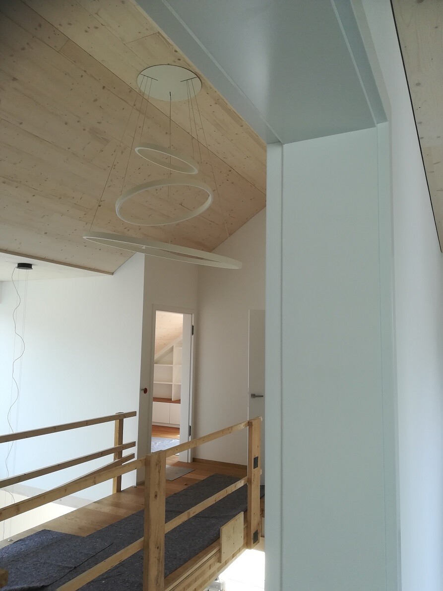 Interior shot of a renovated house: wooden ceiling, railing, modern round lights.