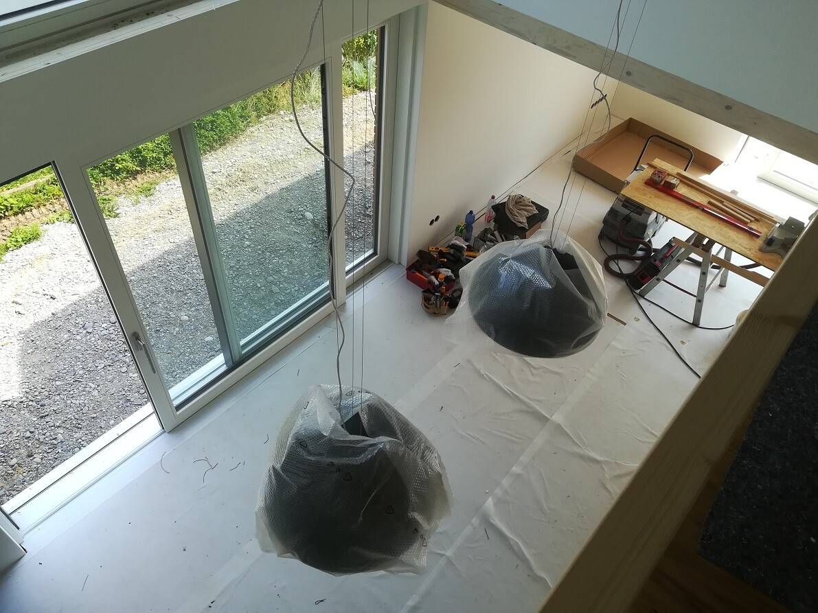 Construction room with large windows; two pendant lights wrapped in bubble wrap, workbench and tools.