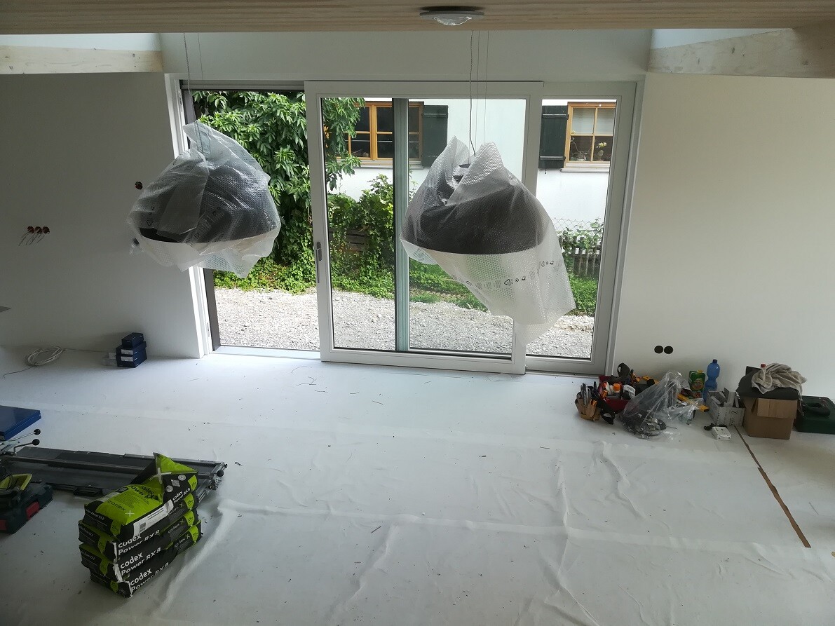 Renovation room with glass sliding door to the garden; two lights under plastic, tools lying around.