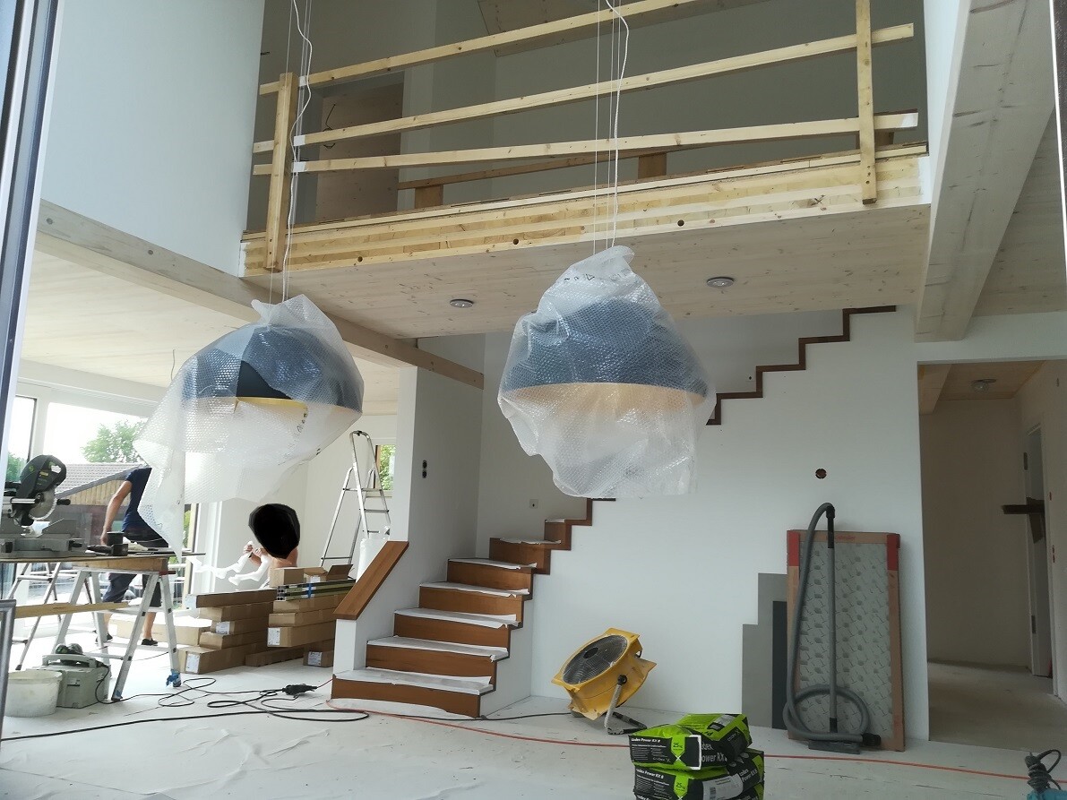 Interior view of a construction site: hanging, wrapped lights, wooden stairs, tools.