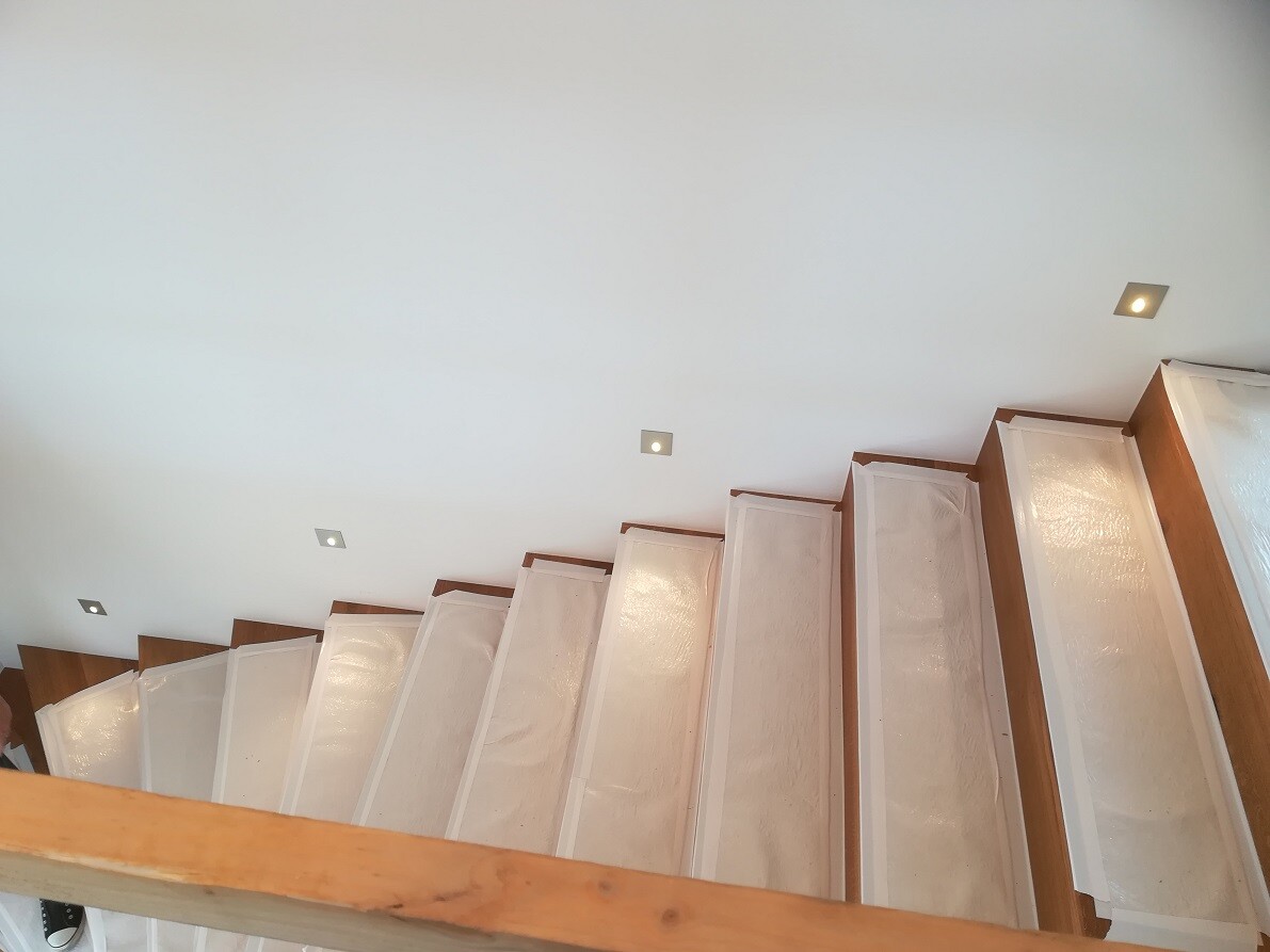 Modern white staircase with brown wooden railing and square recessed ceiling lights.