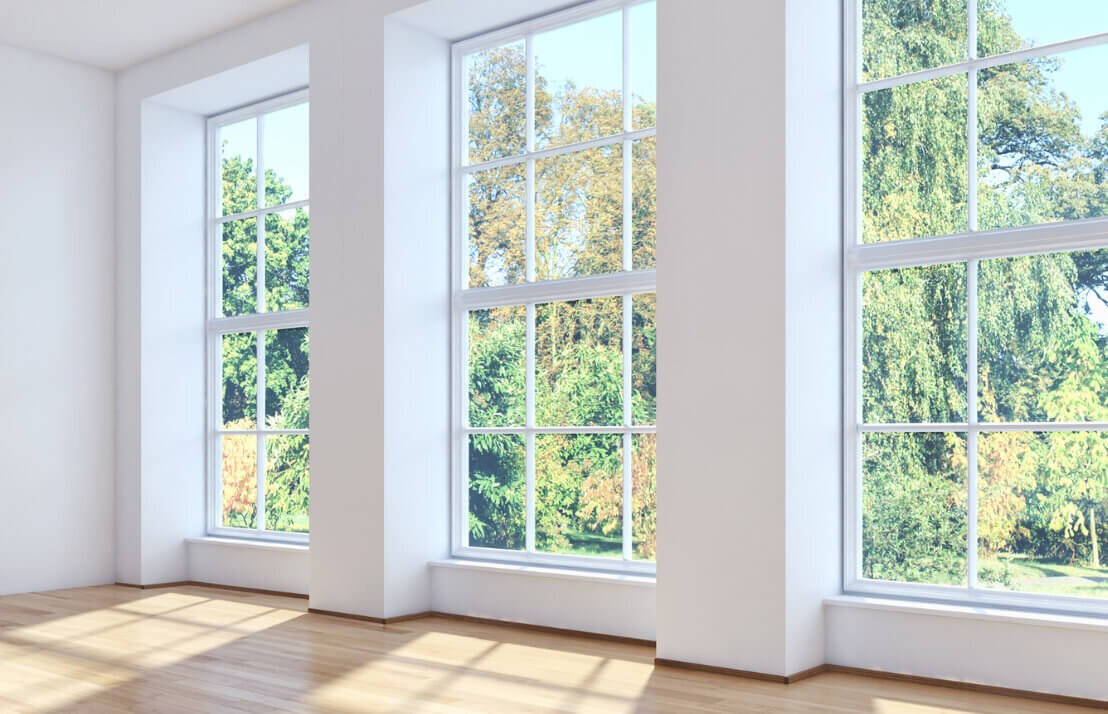 Bright, empty room with large windows, wooden floor and view of green trees.