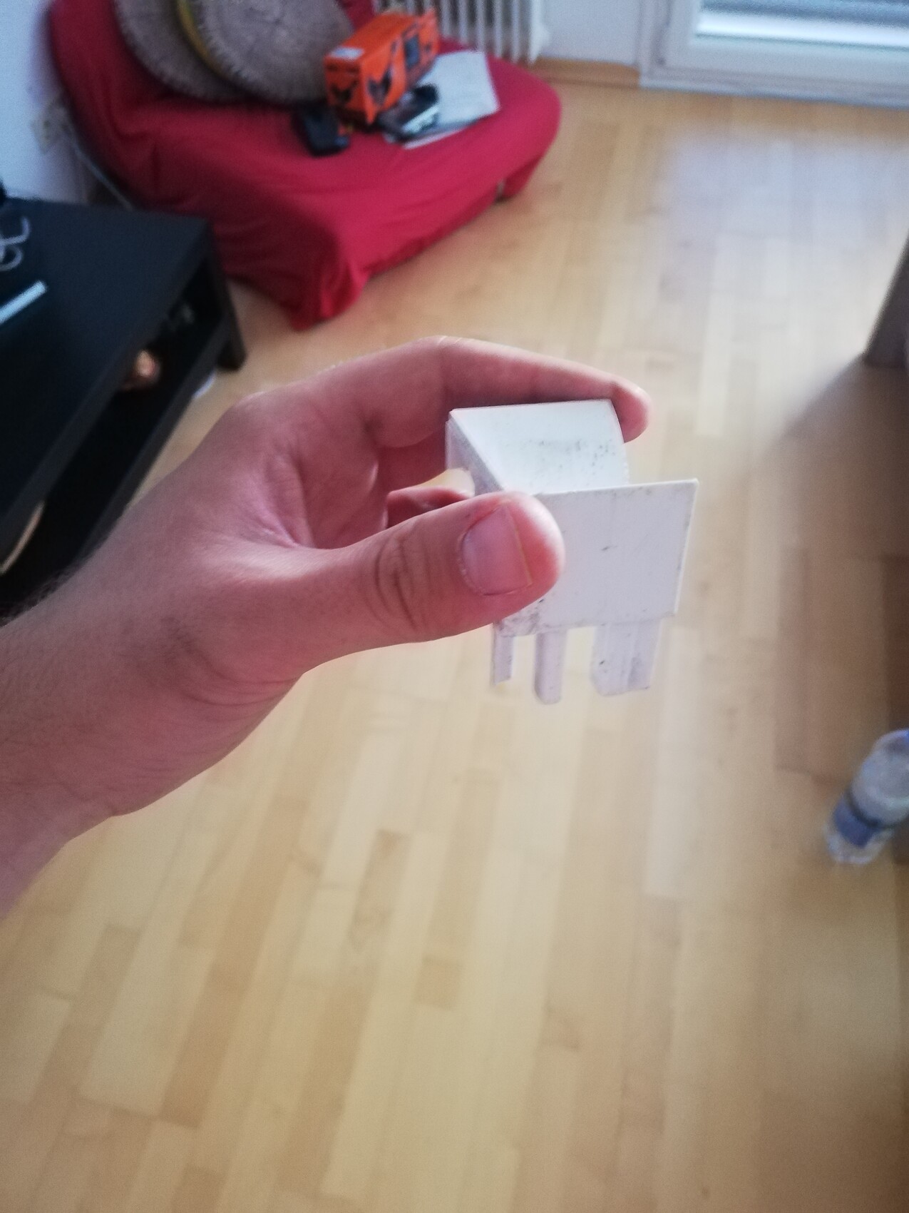 Hand hält weißen Kunststoff-Verbinder mit Stiften in einem Wohnzimmer mit Holzboden