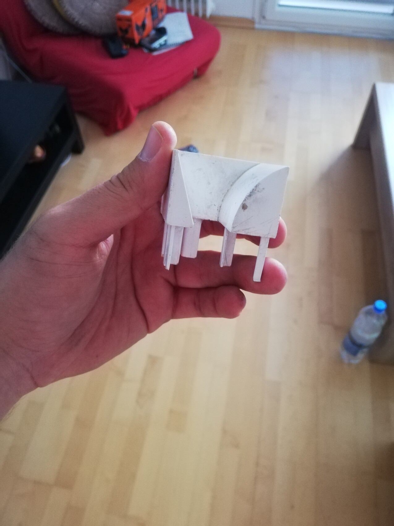 Hand hält kleines weißes Dachstück eines Hausmodells vor Wohnzimmer-Hintergrund