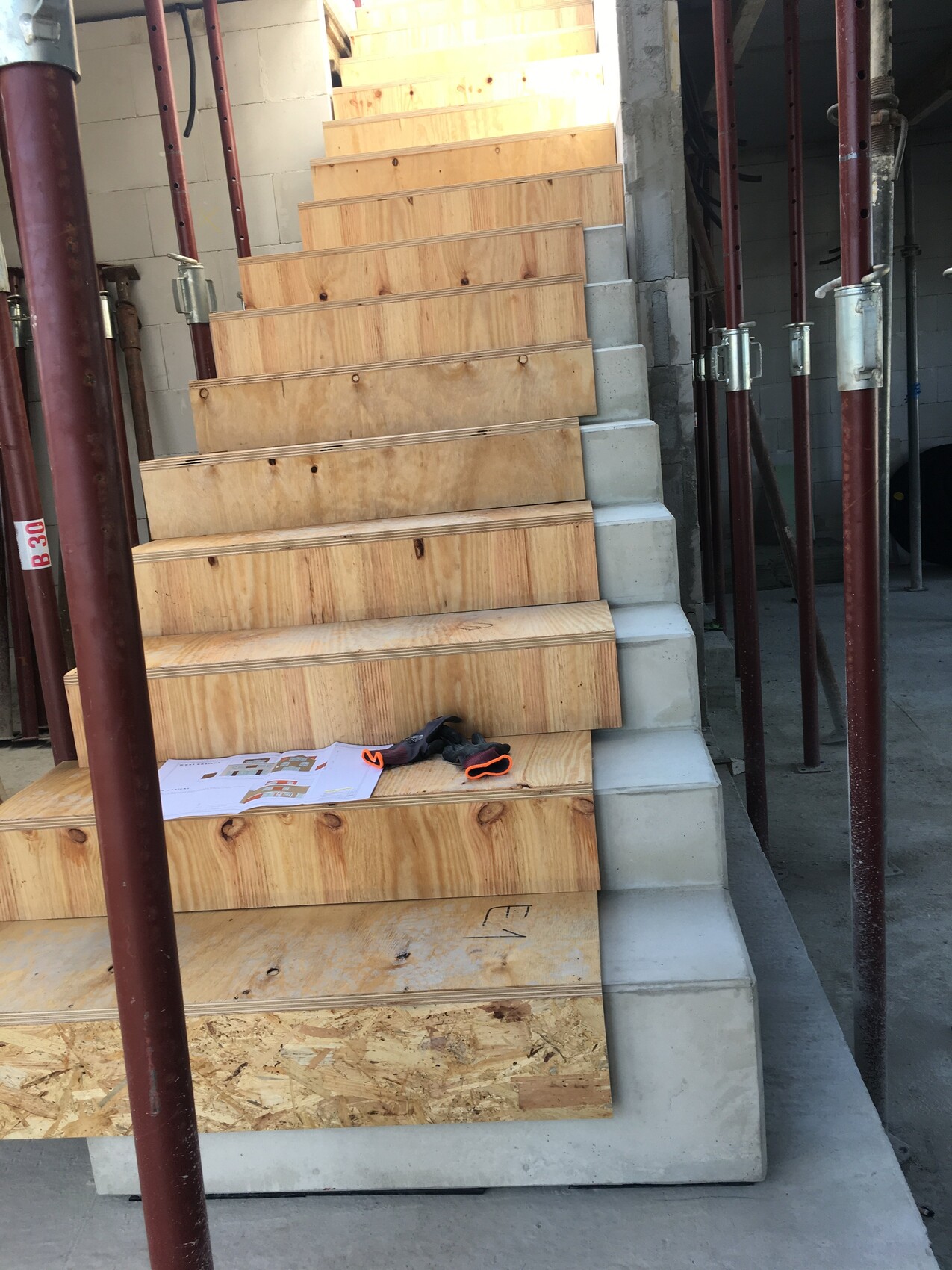 Baustellen-Treppe aus Sperrholzstufen mit Stahlstützen; Handschuhe auf der unteren Stufe.