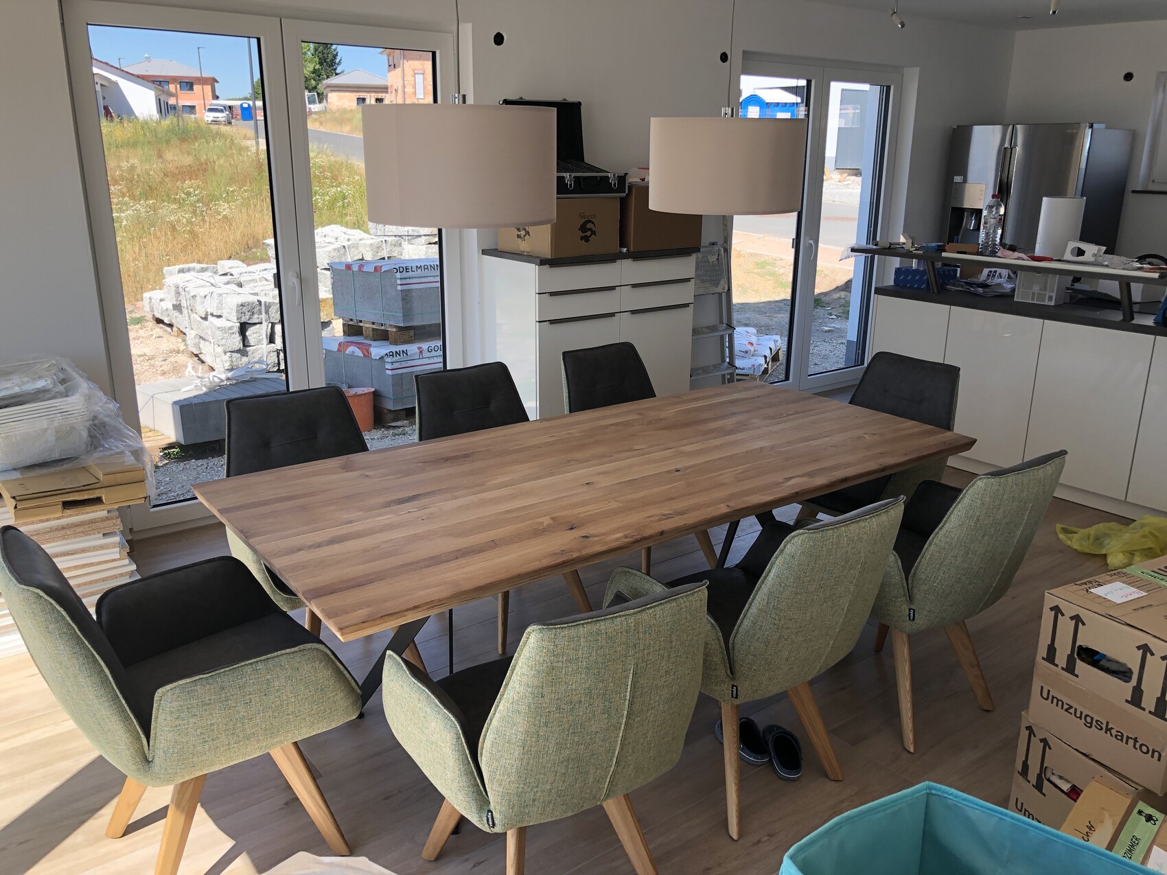 Large wooden table with eight green armchairs; moving boxes and construction materials in the background.