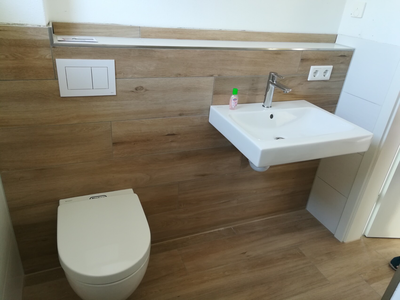 Modern bathroom with wall-mounted sink, chrome faucet, toilet flush tank, wood paneling.