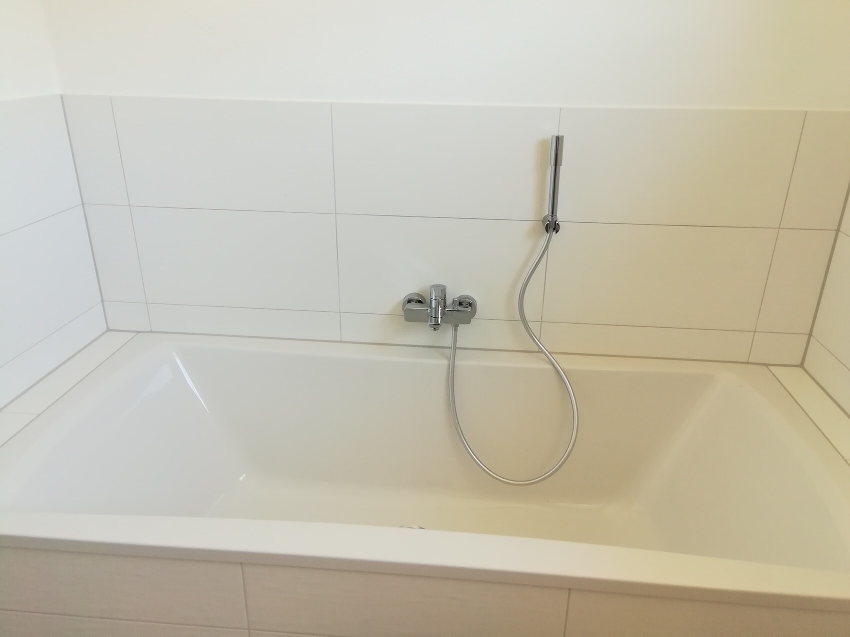 White bathtub with faucet, showerhead, and wall tiles in the bathroom.