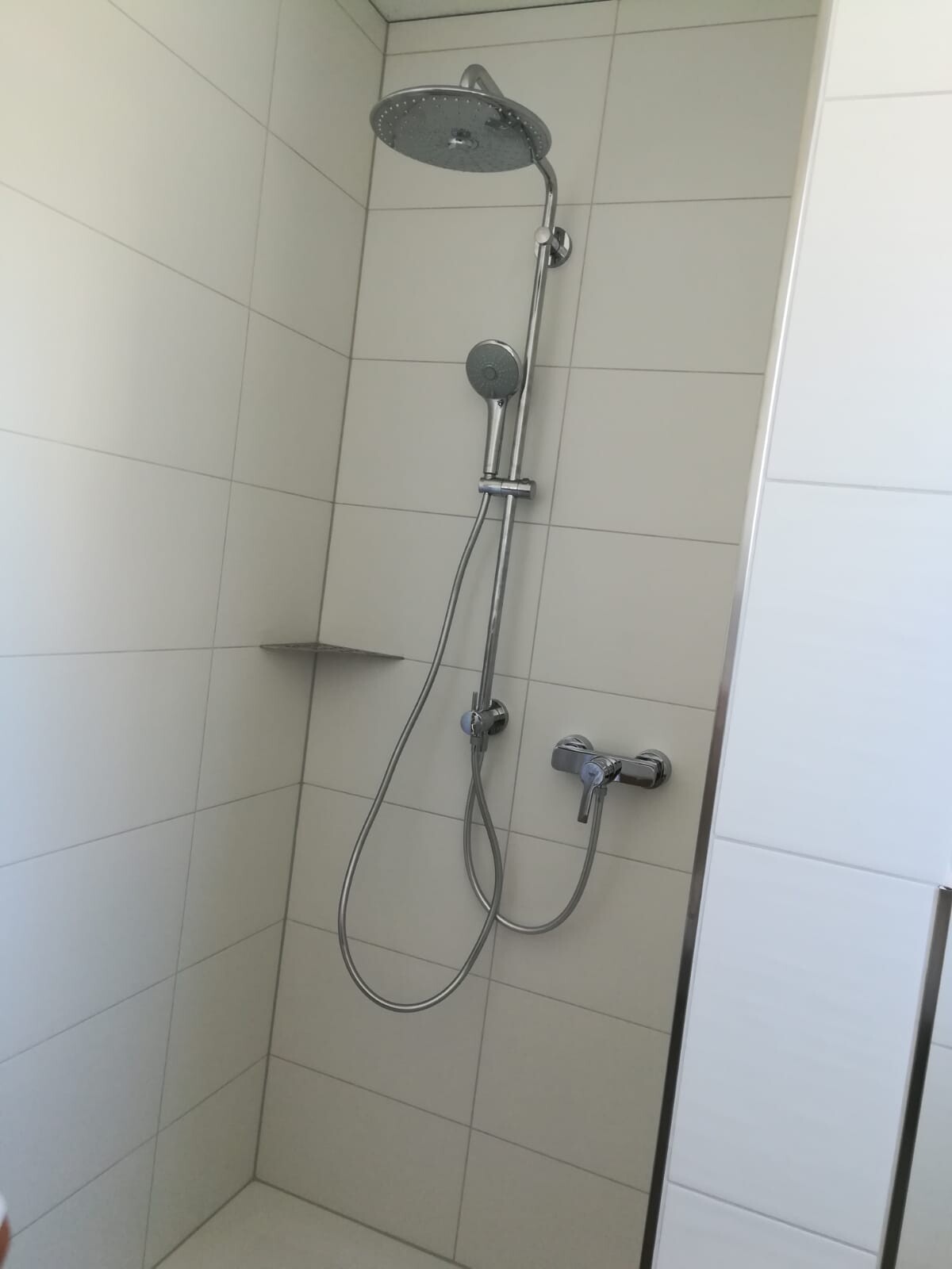 Shower area with large rain showerhead, handheld shower on rail, and tiled wall