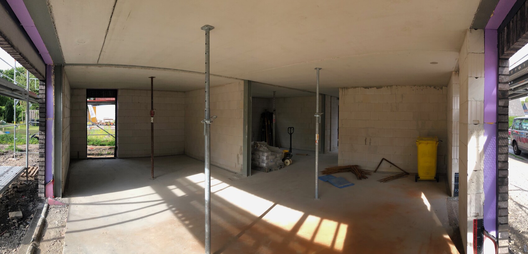 Innenraum einer Baustelle: Unverputzter Raum mit Metallstützen, Bauwerkstoffen und Gelber Mülltonne