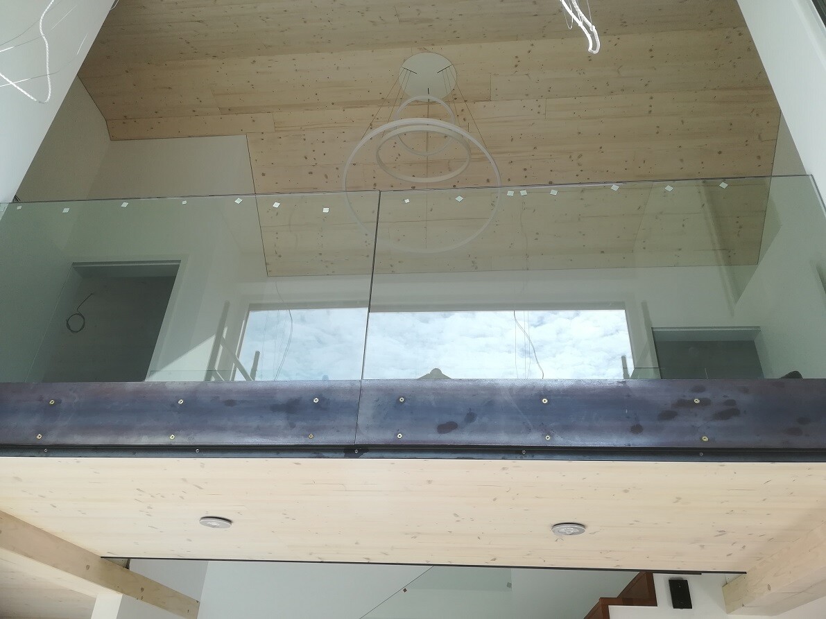 Modern loft apartment with glass railing, wooden ceiling, and circular pendant light.