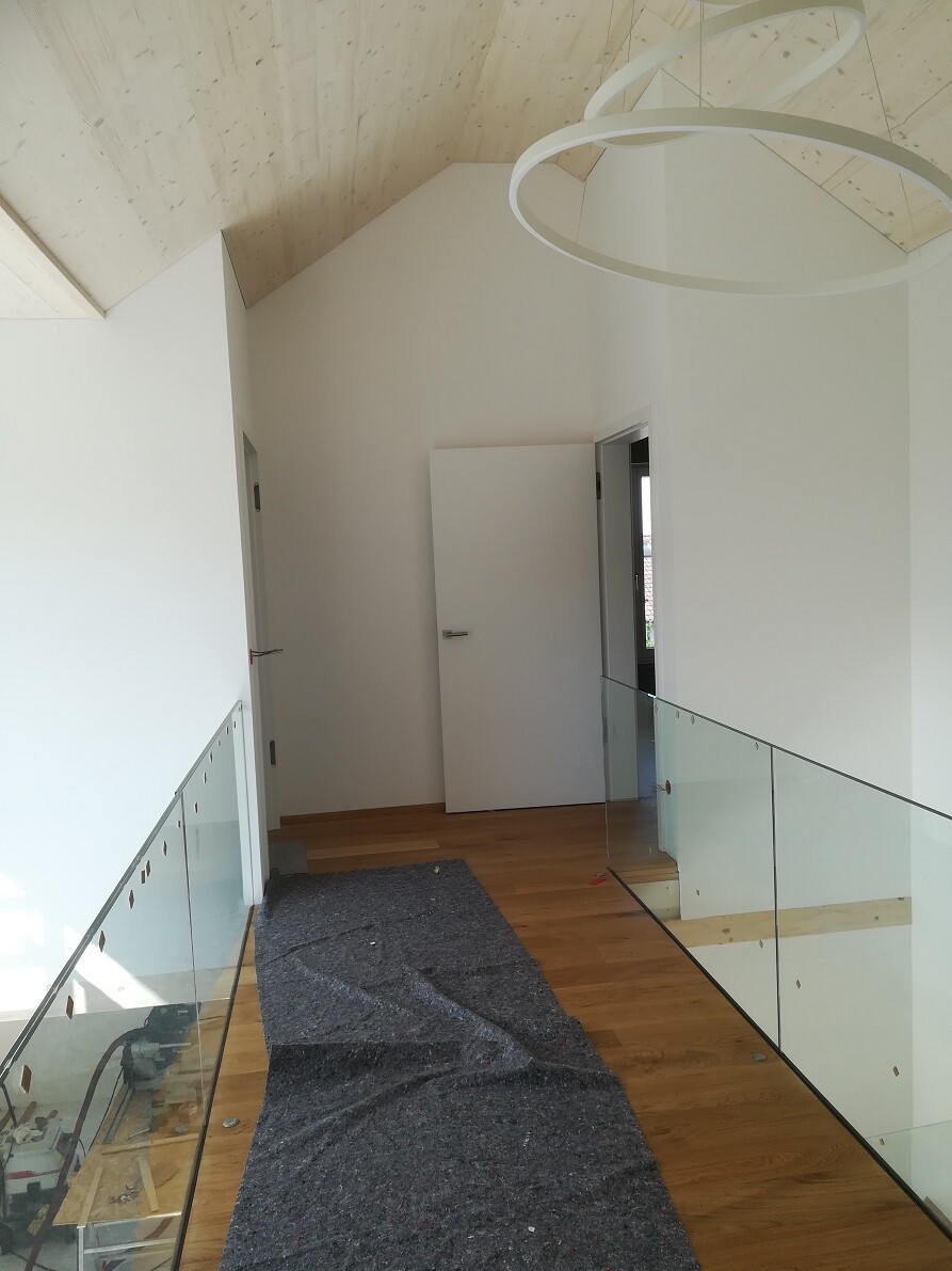 Bright hallway with wooden floor, glass railing, white walls, and round ceiling lights.