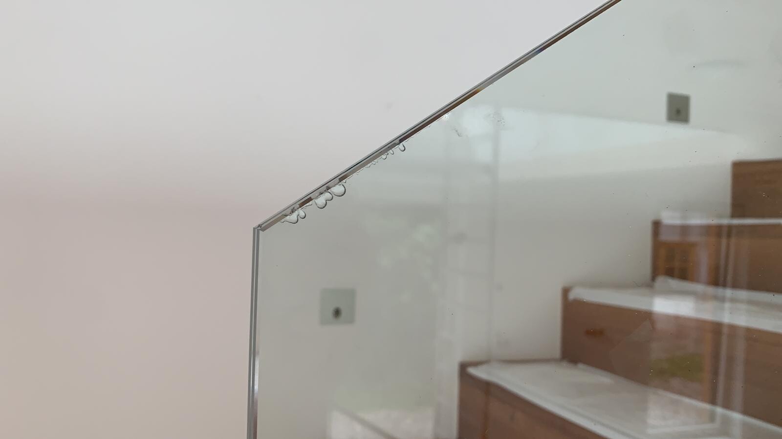 Diagonal glass panel with water droplets at the edge, view of stairs in the room