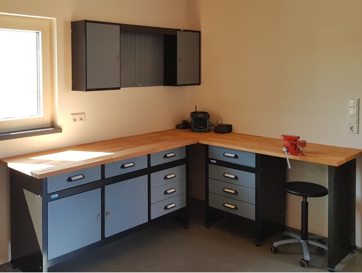 Workshop corner with wooden worktop, gray drawers, wall cabinet, and window on the left.
