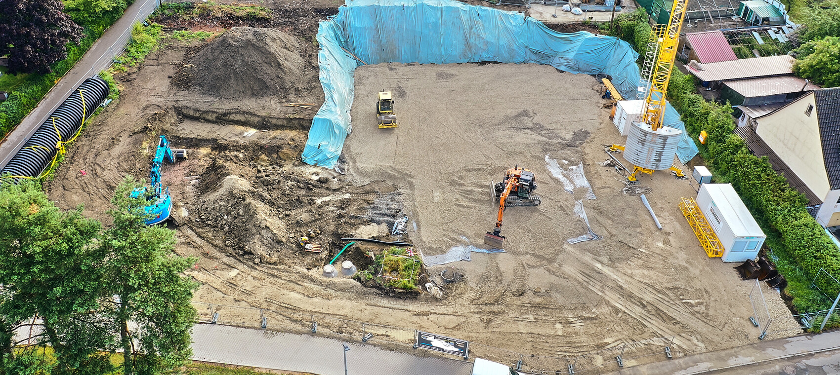 Aerial view of an excavation site with excavators, crane, blue tarp covering, and construction machinery.